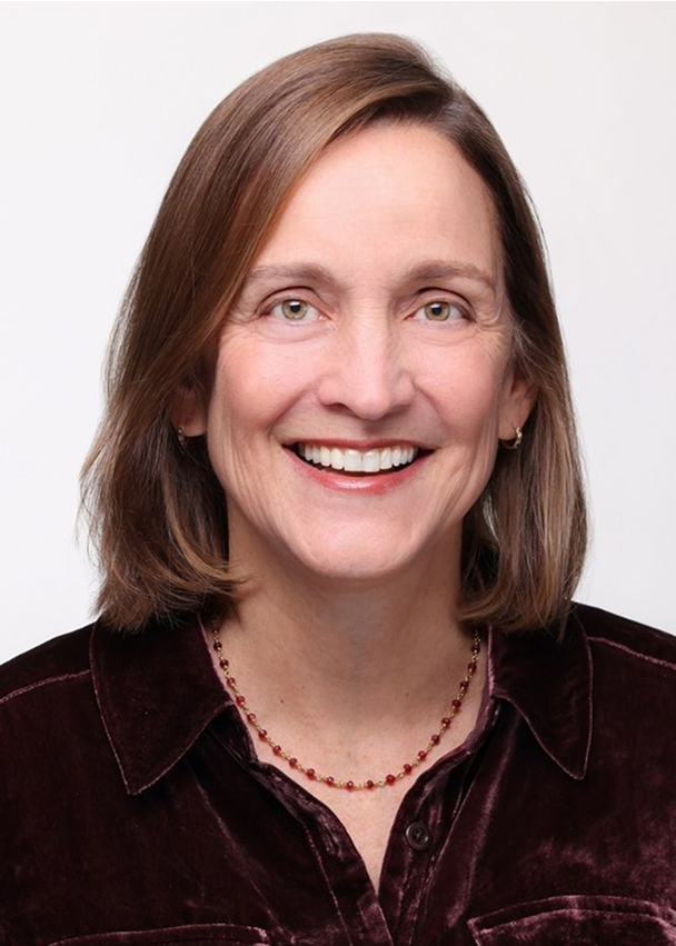 A woman with shoulder-length brown hair, wearing a maroon velvet shirt and a beaded necklace, smiling at the camera against a plain light background.