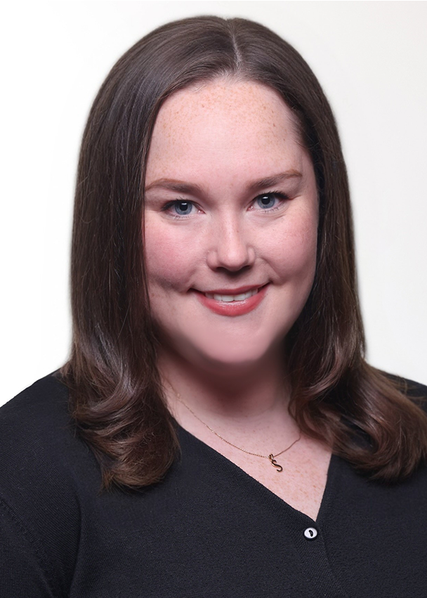 Sarah Kennedy, a woman with straight brown hair, wearing a black top and a necklace, is smiling at the camera against a plain white background.