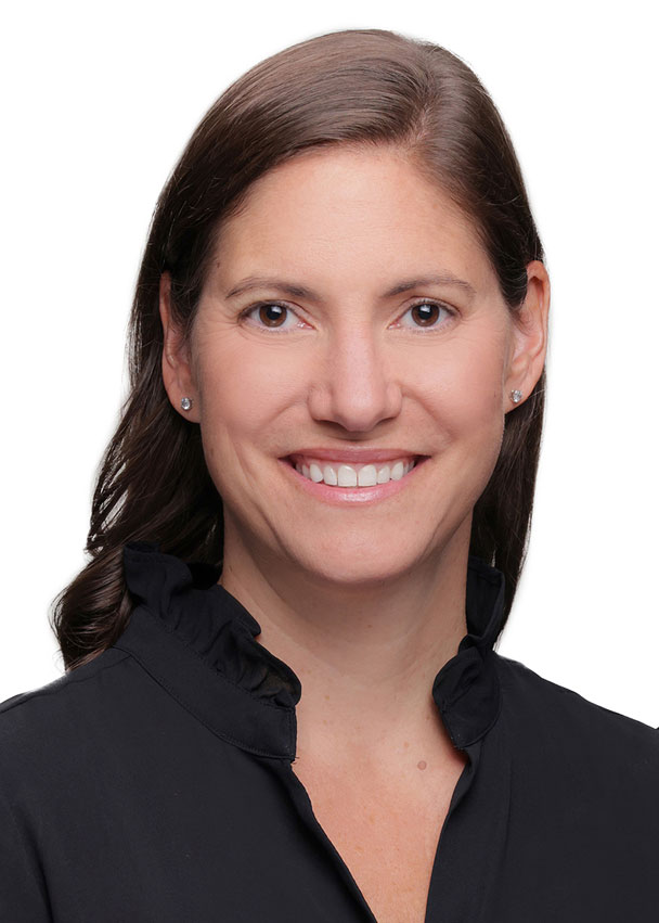 Smiling woman with straight brown hair, wearing a black top with a ruffled collar, photographed against a plain white background—Katherine Gehrmann.